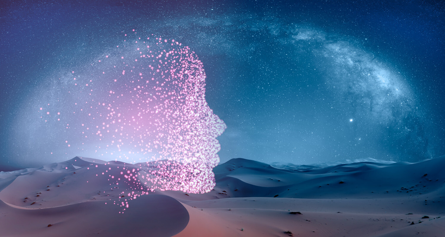 A digital face silhouette composed of glowing pink particles blending into a starry night sky over a desert landscape, symbolising the integration of artificial intelligence with natural environments.