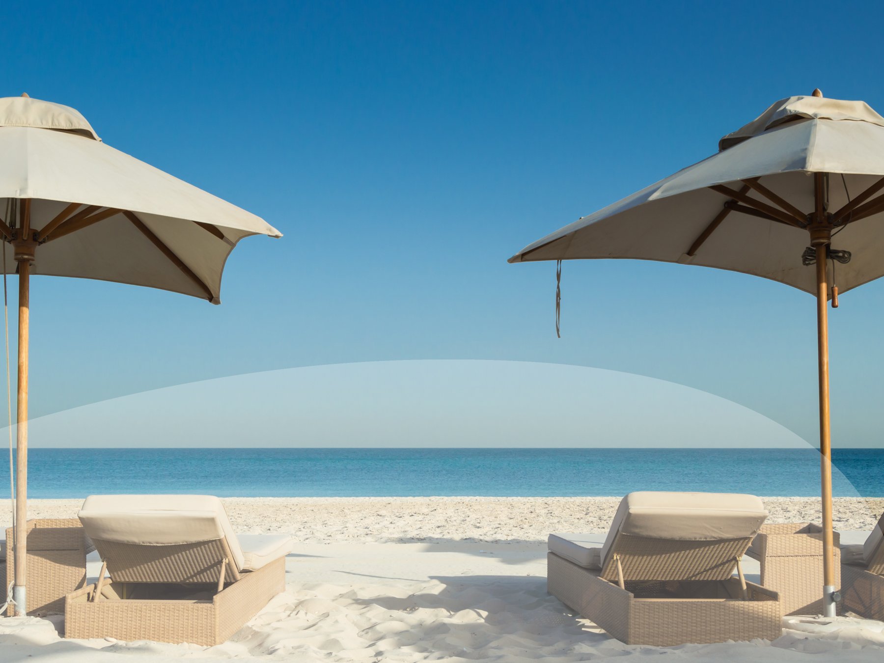 Beach umbrellas at a beautiful white beach in Abu Dhabi, UAE. The sea and a clear blue sky in the background.