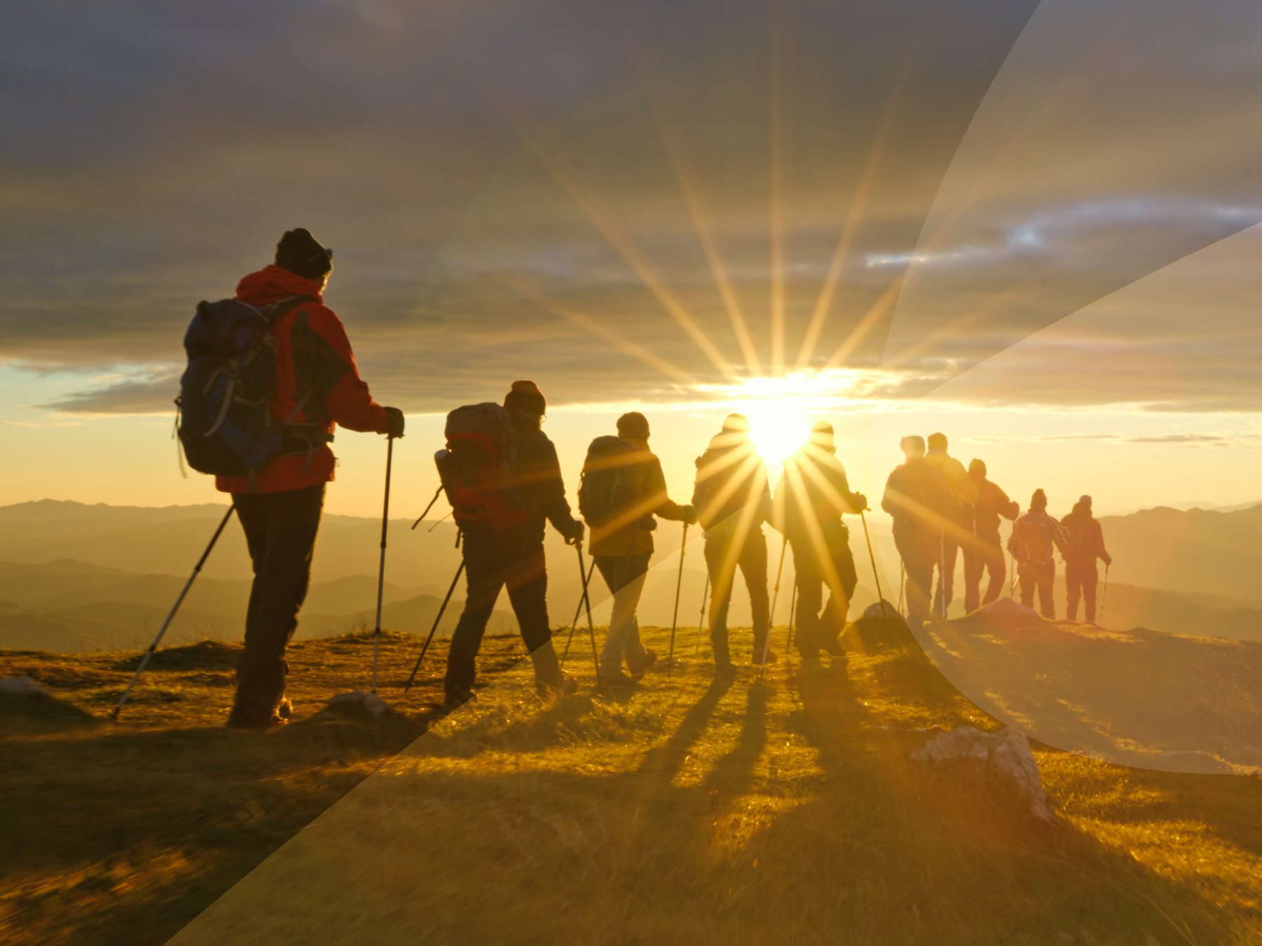 A group of people trekking in the mountains, walking towards the sunset.