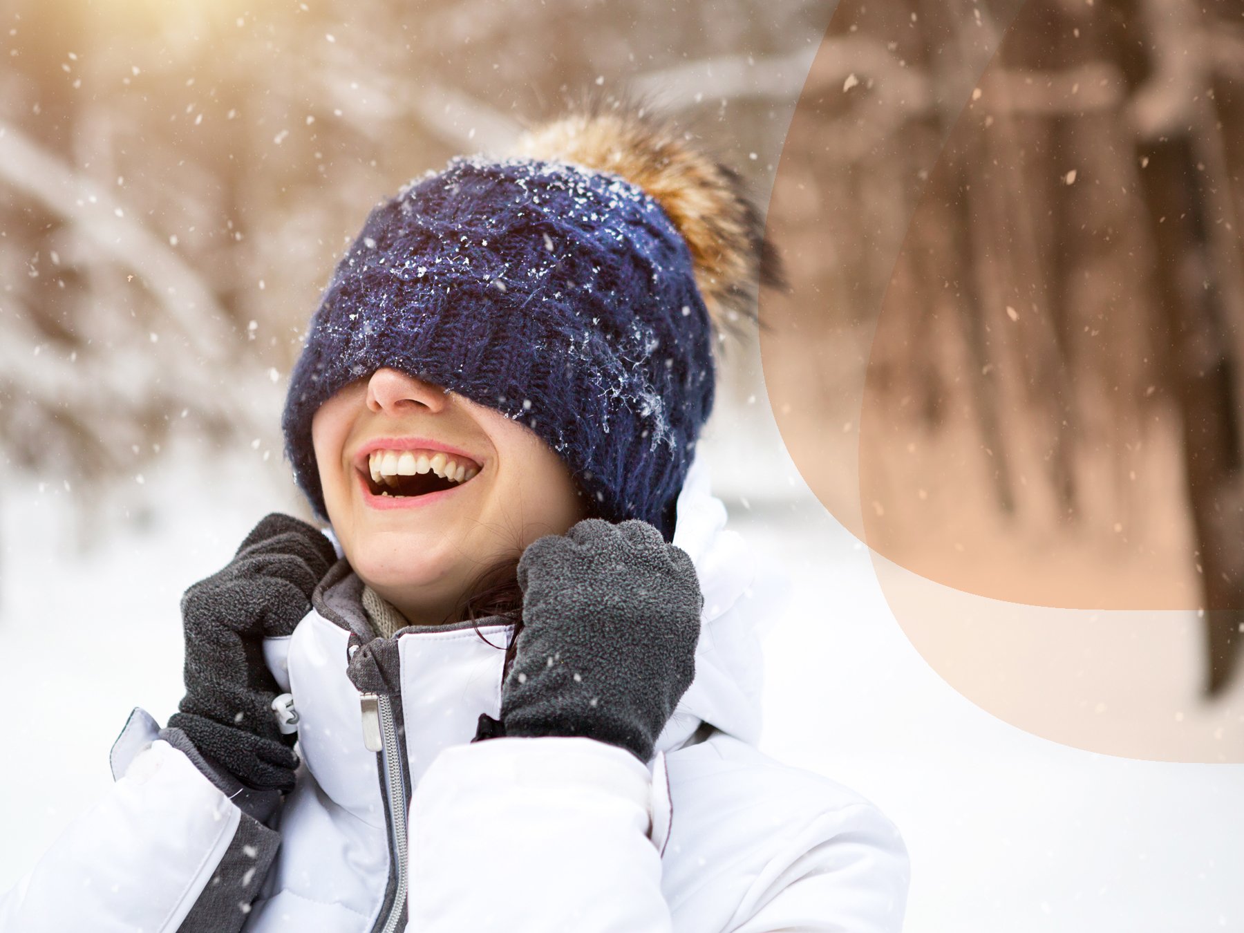 Close-up of a smiling woman with a knitted hat pulled over her eyes, enjoying the snow in the spring sun.