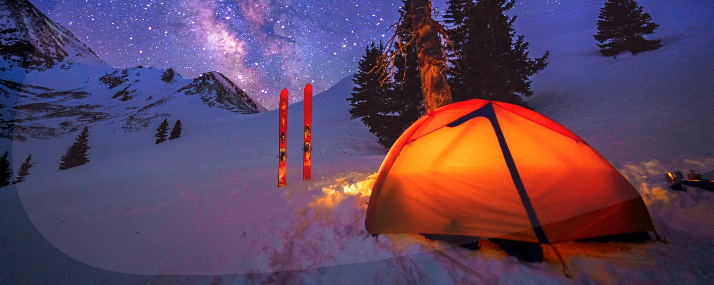 Ski camp setup with glowing tent at high altitude under mountain ridge with stars and Milky Way Galaxy.
