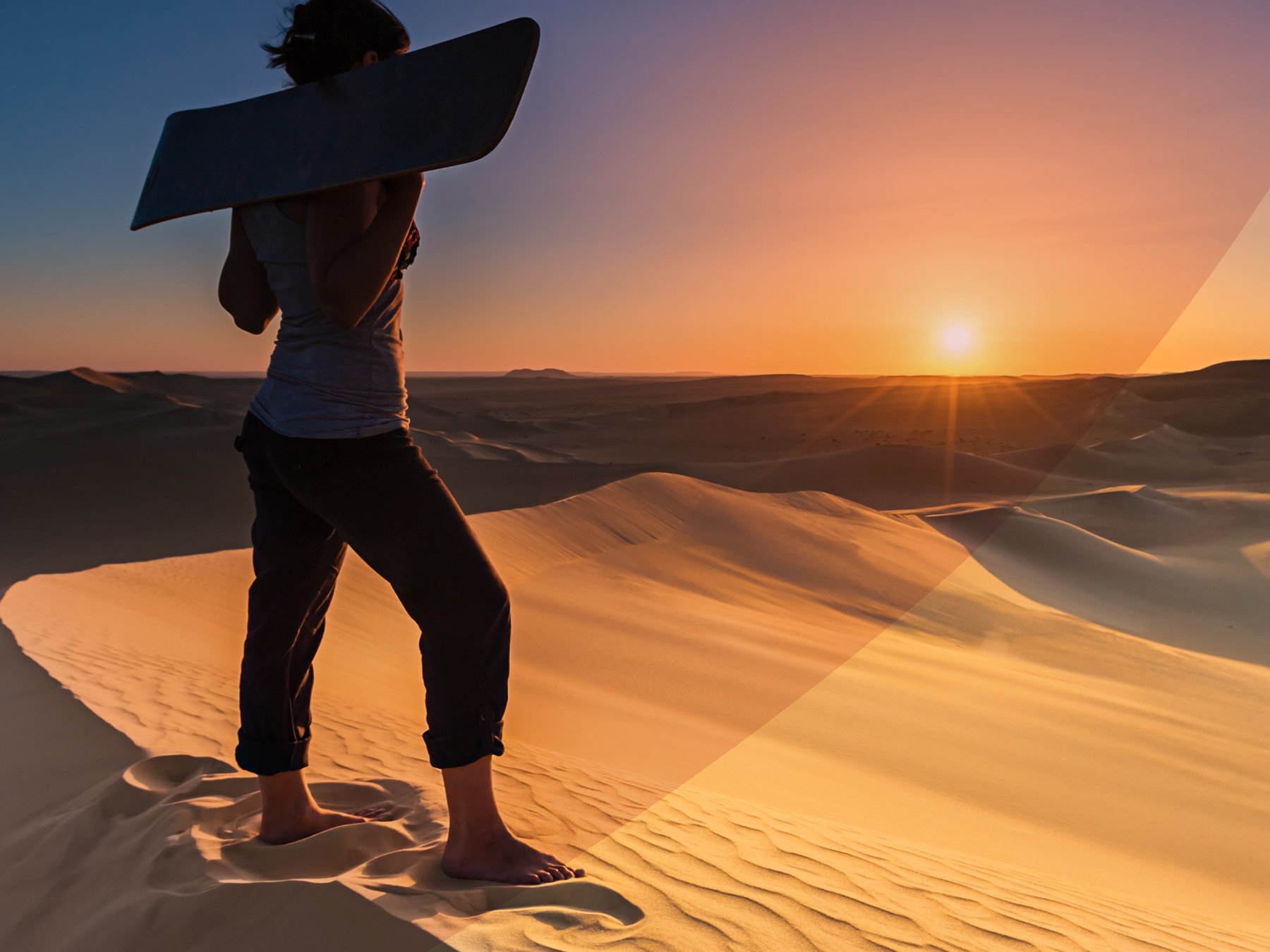 Young woman standing barefoot on sand dunes, holding a sandboard and watching the sunset in The Sahara Desert. Close-up.