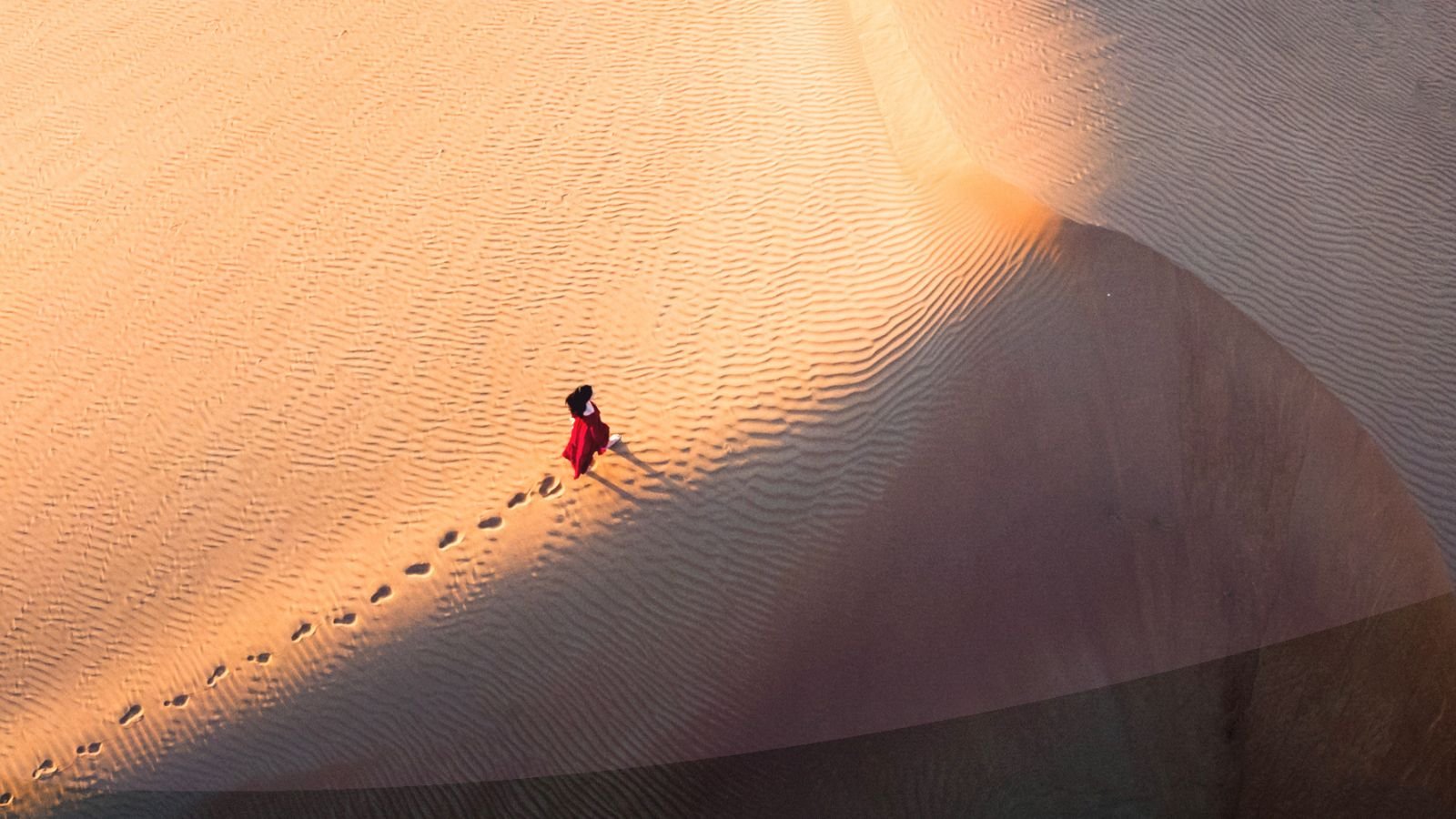 Woman walking in the desert during sunset aerial view.