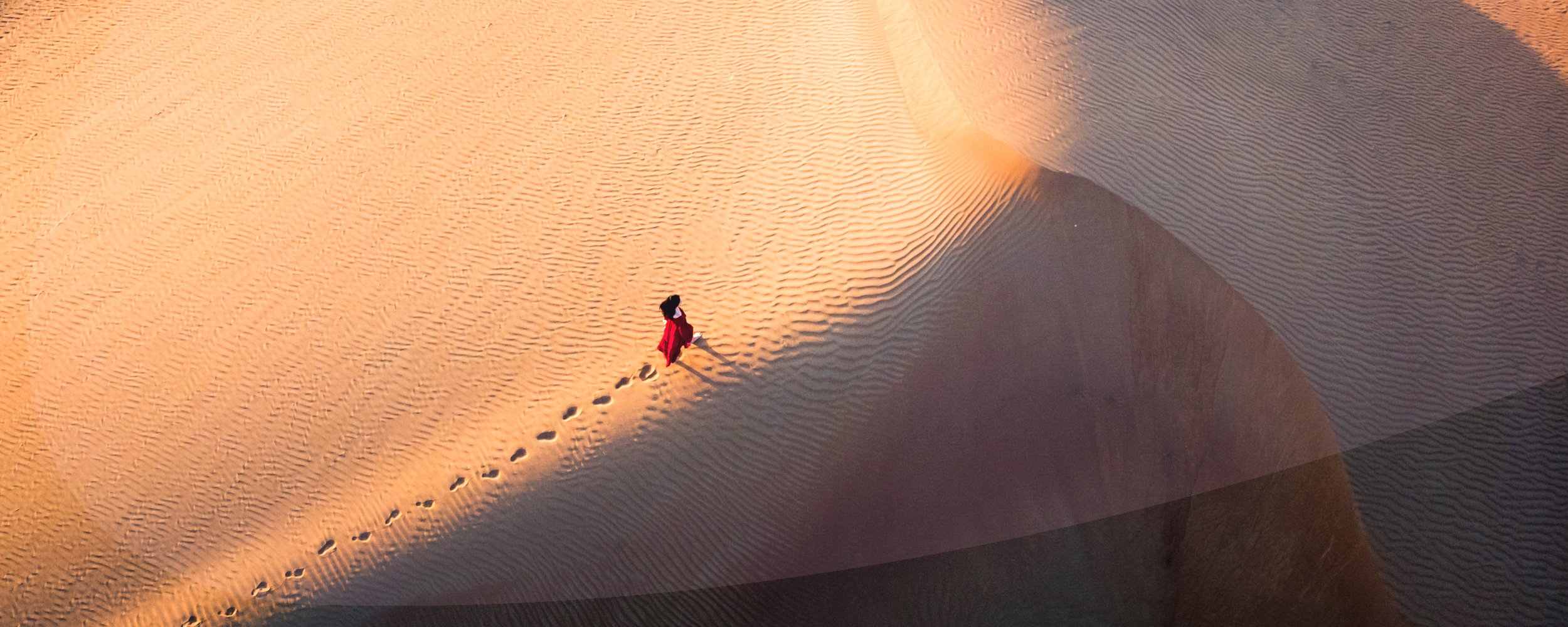 Woman walking in the desert during sunset aerial view.