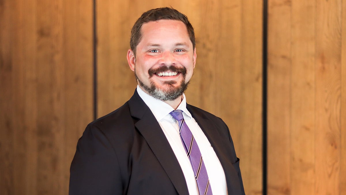 Johnny Kollin in business attire, smiling, a wooden wall behind him.