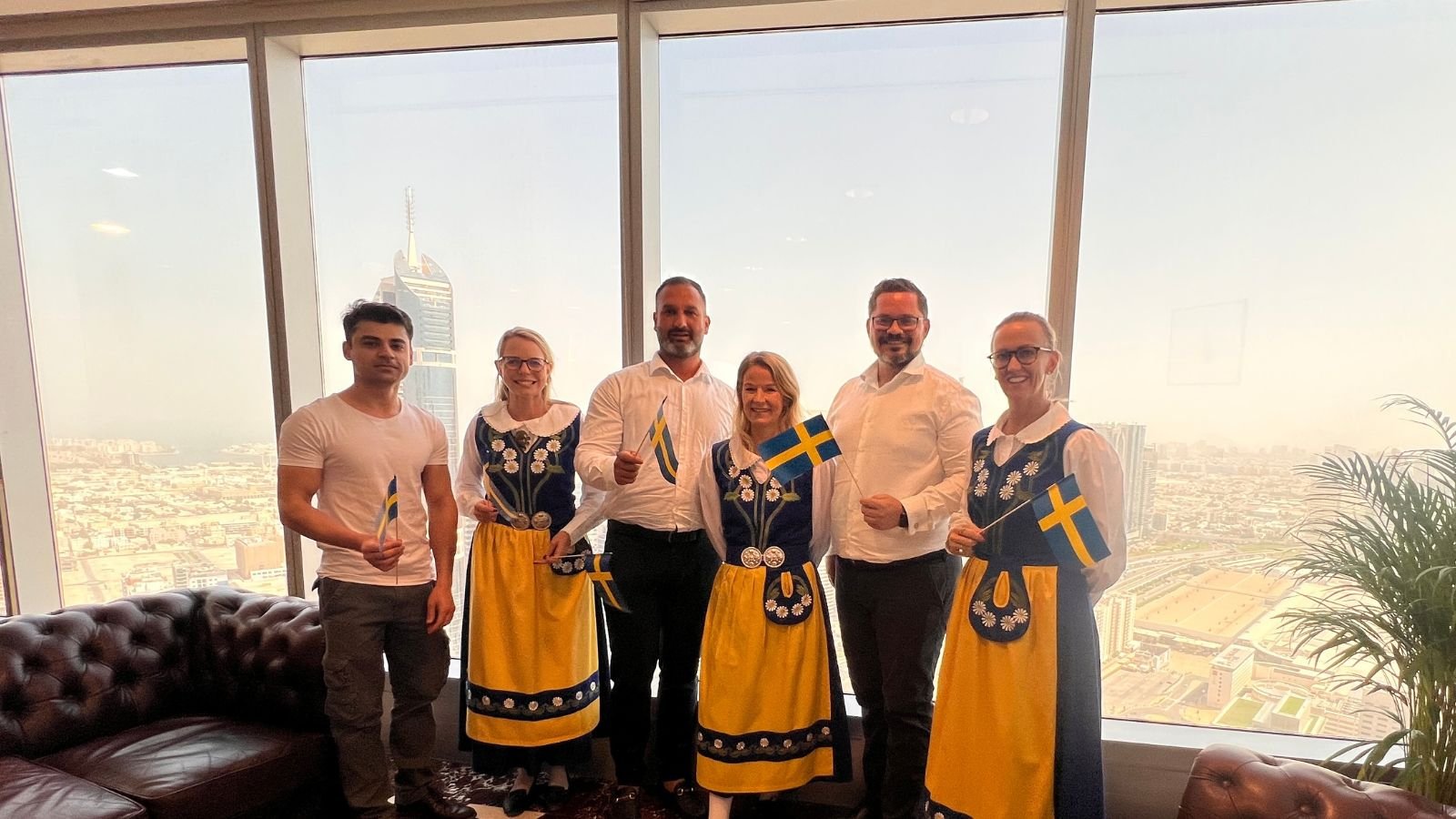 Swedish Business Council UAE directors dressed in Swedish national dresses visit the Várri Consultancy team. They're holding small Swedish flags.
