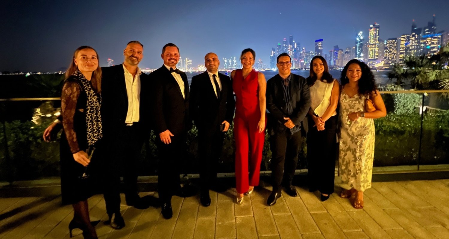 A group photo of all Várri Consultancy's esteemed guests during the welcome drinks reception at the Swedish Business Council's annual Julbord. The guests are elegantly dressed, standing against the stunning backdrop of Dubai's illuminated skyline.