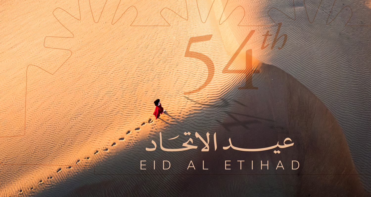 Eid Al Etihad 2025 greeting card by Várri Consultancy featuring golden desert sands with footprints, the number 54, and Arabic script for Eid Al Etihad framed by a sunburst motif, symbolising heritage, resilience, and progress.